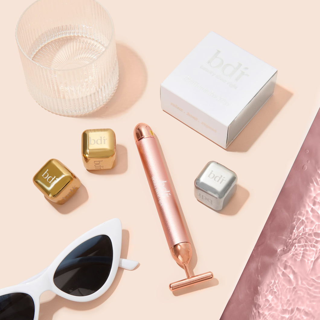 Sunglasses sit next to rose gold sculpting massager with platinum and gold ice dice 