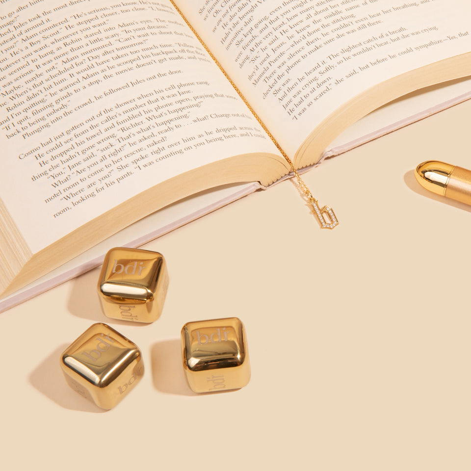custom pendant necklace sits in open book with 24k gold sculpting massager and gold ice dice
